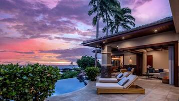 A modern house with a pool, outdoor seating, and a view of the ocean at sunset.