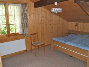 Ein Zimmer mit Holzboden, einem Bett, einem Stuhl, einem Fenster mit Vorhängen und einem Deckenventilator.