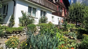 A traditional chalet with a sloped roof, wooden balcony, and a garden with various plants and flowers. - Apartment Aelpli by Interhome (Grindelwald)