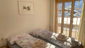 Een tweepersoonskamer met twee bedden, een raam met gordijnen, een lijst met foto aan de muur en een nachtkastje.