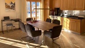 Een moderne keuken met houten kasten, een eettafel met stoelen, een fornuis en een laptop op een bureau.