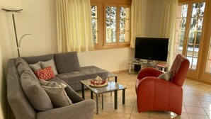 Een woonkamer met een grijze bank, een rode fauteuil, een salontafel en een televisie.