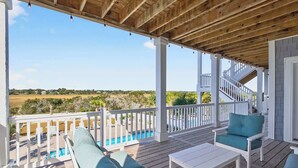 A covered outdoor area with a pool, wooden deck, white railings, and outdoor furniture. - Isle Have Another by Brunswick Vacation Rentals: 7BR w/ Elevator, Pool & Views! (Ocean Isle Beach)