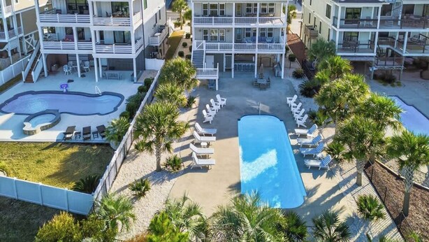A resort with multiple-story buildings, a swimming pool, and lounge chairs. - Isle Be Back by Brunswick Vacation Rentals: Oceanfront, Pool, Elevator & Views! (Ocean Isle Beach)