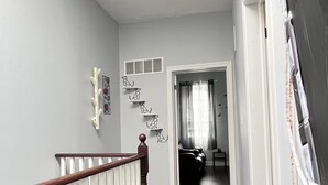 Un couloir avec un escalier en bois, un radiateur blanc et une porte donnant sur une autre pièce.