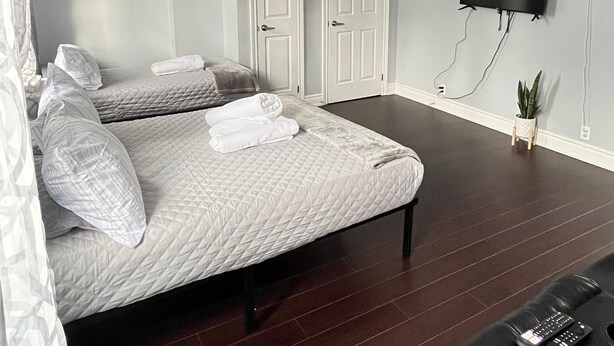 Une chambre à coucher avec un lit, un téléviseur fixé au mur et une petite plante posée sur le sol.