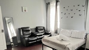 Une chambre à coucher avec un lit, deux fauteuils en cuir noir, un grand miroir et des autocollants décoratifs représentant des papillons sur les murs.