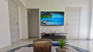 A modern living room with a large flat-screen TV mounted on the wall, a wooden floor, and a small potted plant on a beige rug. - Gemütliche 2-Schlafzimmer-Wohnung mit Meerblick, Crikvenica by Interhome (Crikvenica)