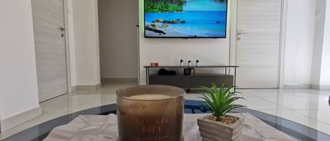A modern living room with a large flat-screen TV mounted on the wall, a wooden floor, and a small potted plant on a beige rug.