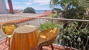 A balcony with a table and two chairs, a railing, and a view of the sea and buildings. - Gemütliche 2-Schlafzimmer-Wohnung mit Meerblick, Crikvenica by Interhome (Crikvenica)