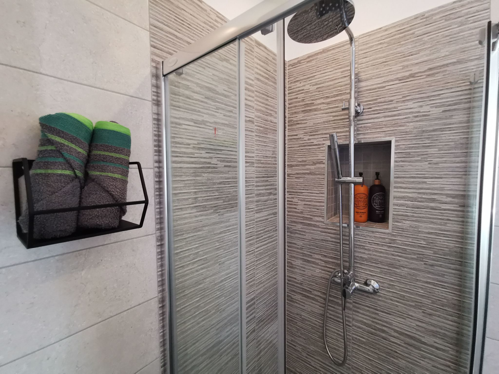 A shower area with a glass door, a towel rack with towels, and a shelf with toiletries.