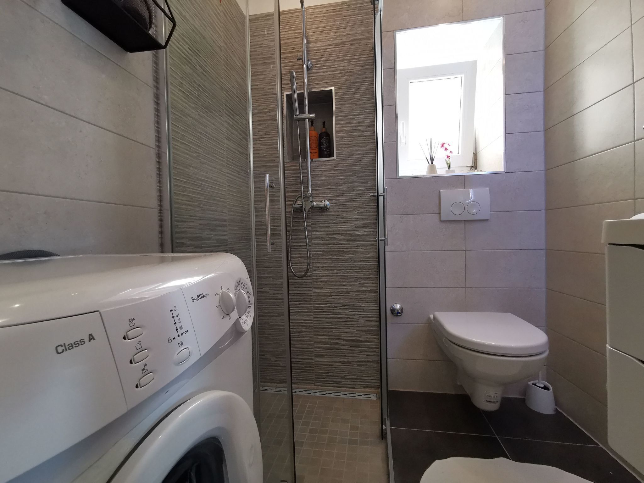 Une salle de bain moderne avec une douche à parois de verre, des toilettes et un lave-linge.
