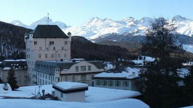 Un edificio histórico con una torre destacada, rodeado de montañas y árboles cubiertos de nieve.