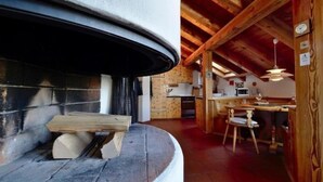 Una cocina rústica con vigas de madera, una chimenea de piedra y un comedor con mesa y sillas de madera.