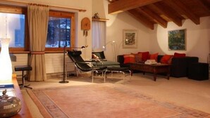 Una sala de estar acogedora con techo de madera, una mesa de comedor con sillas, un sofá con cojines rojos y una ventana con cortinas.