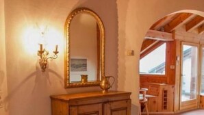 Un mueble de madera con un espejo grande, una silla y una alfombra estampada en una habitación con suelo de baldosas y techo abovedado.