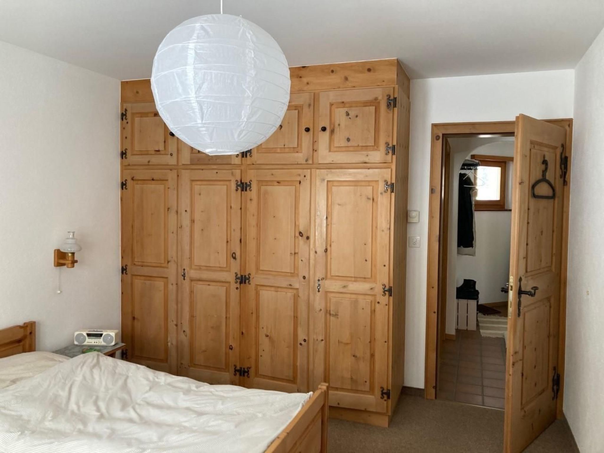 Une chambre avec une armoire en bois, un luminaire suspendu, une radio et un lit.