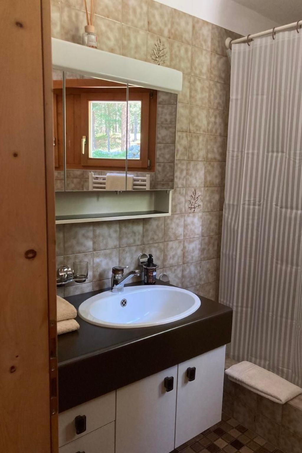 Un baño con un lavabo blanco, un espejo encima y una ventana con vistas a la vegetación.