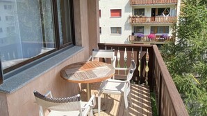 Un balcone con tavolo in legno e sedie bianche, affacciato su una zona montuosa.