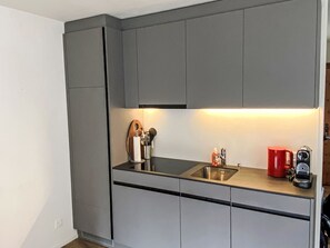Een moderne keuken met grijze kastjes, een roestvrijstalen spoelbak en een rode waterkoker.