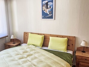 Une chambre à coucher avec un lit, deux tables de chevet, une commode, une affiche au mur et une fenêtre.