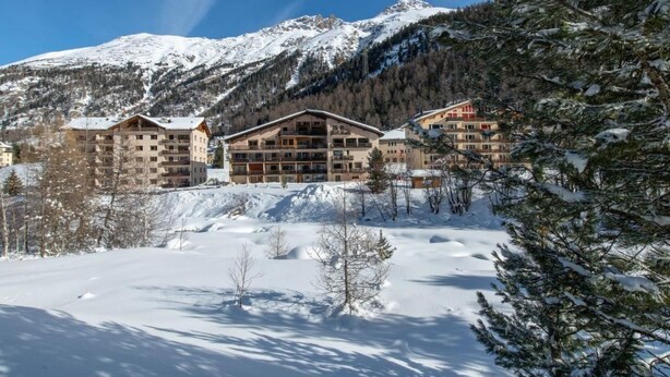 A snow-covered mountain resort with multiple buildings, including a large lodge with balconies and a smaller building with a sloped roof. - Chesa la Furia WHG 24 by Interhome (Pontresina)