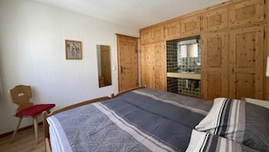 A bedroom with a large bed, wooden wardrobe, and a small chair. - Chesa la Furia WHG 24 by Interhome (Pontresina)