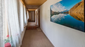 A corridor with a wooden ceiling, a large painting of a lake, and a patterned rug. - Chesa la Furia WHG 24 by Interhome (Pontresina)