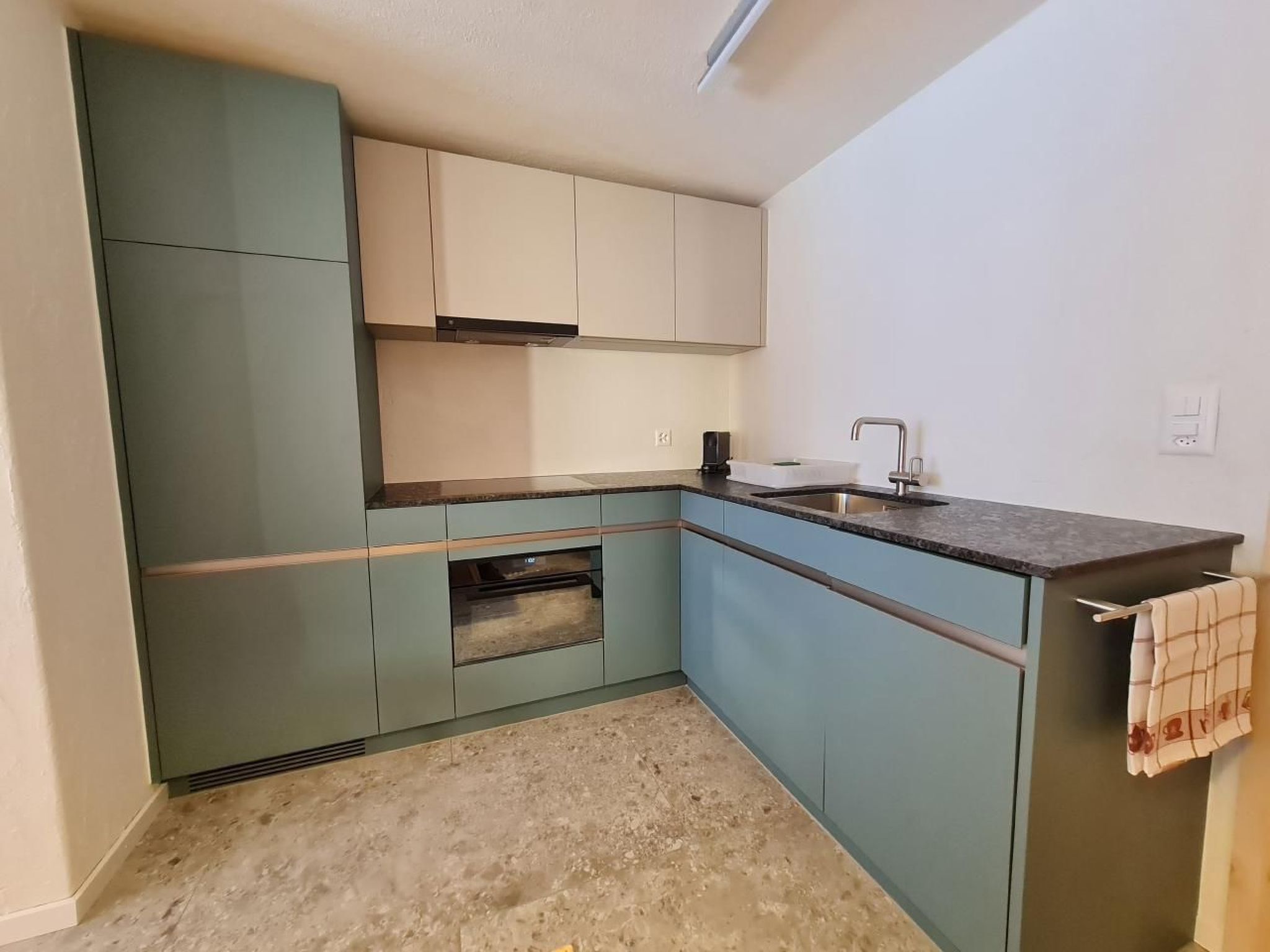Una cocina compacta con armarios azul claro, encimera oscura y horno integrado.