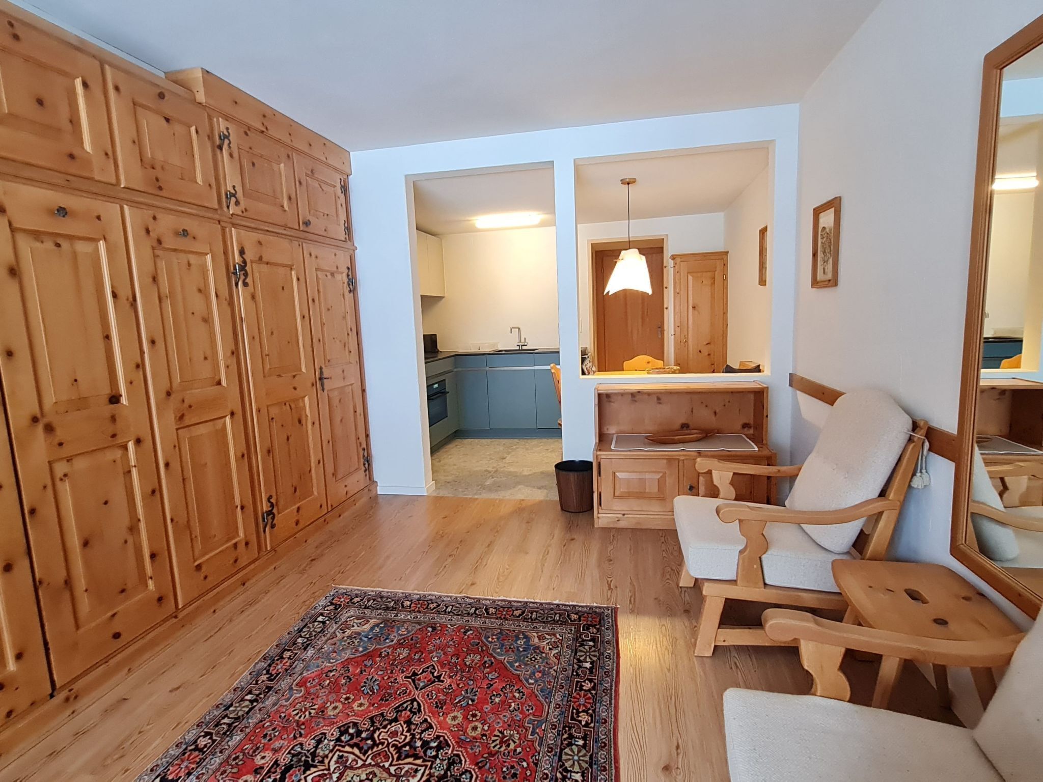 Una habitación amplia con armarios de madera, una mecedora, una alfombra y vistas a una zona de cocina.