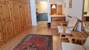 Une pièce spacieuse avec des meubles en bois, un fauteuil à bascule, un tapis et une vue sur un coin cuisine.