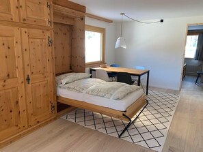 Una habitació amb un llit, un escriptori i una cadira. Hi ha una finestra i una làmpada penjant.