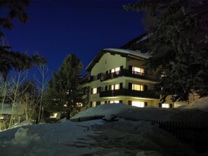 A multi-story hotel with balconies, surrounded by snow-covered ground and trees. - Chesa Andrea, EG by Interhome (Pontresina)