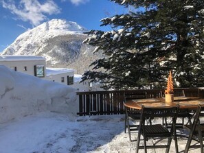 A snow-covered outdoor area with a wooden table and chairs, a snow-covered mountain in the background, and a building with a white facade. - Chesa Andrea, EG by Interhome (Pontresina)
