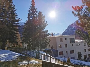 A building with a snow-covered roof, surrounded by tall trees and mountains in the background. - Chesa Andrea, EG by Interhome (Pontresina)