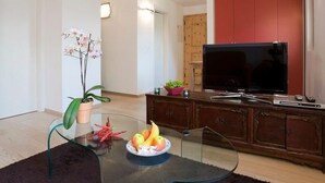 Een woonkamer met een glazen salontafel, een schaal fruit, een potorkidee, een flatscreen televisie en een houten kast.