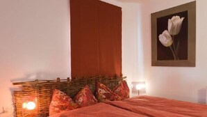 Een slaapkamer met een groot bed, een hoofdbord met een geweven patroon, twee bedlampjes en een lijst met een bloemenafbeelding aan de muur.