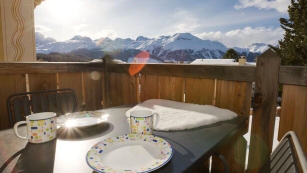 Een houten terras met een gedekte tafel voor twee, met uitzicht op een besneeuwd berglandschap.
