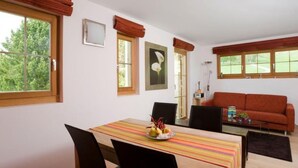 Een zithoek met een tafel, stoelen en een schaal fruit. Achtergrond heeft een bank en een lamp.