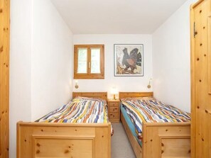 Une petite pièce chaleureuse, avec deux lits en bois, une fenêtre et un tableau encadré au mur.