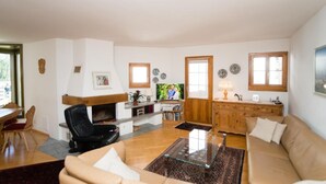 A living room with a sofa, a glass coffee table, a fireplace, a television, and a wooden cabinet. - Chesa Aquileja Trüb by Interhome (Pontresina)