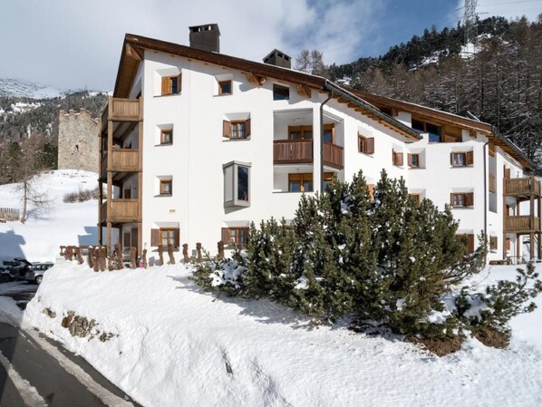 Un immeuble à plusieurs étages doté de balcons, entouré de neige et d’arbres.