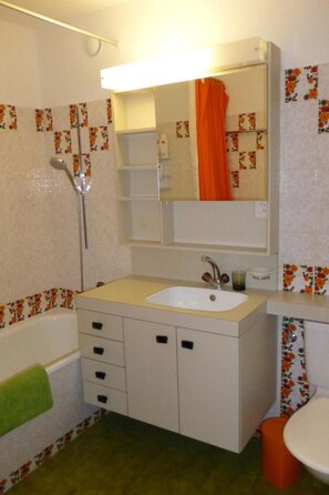 Een badkamer met een wit wastafel, spiegel, douche en toilet.