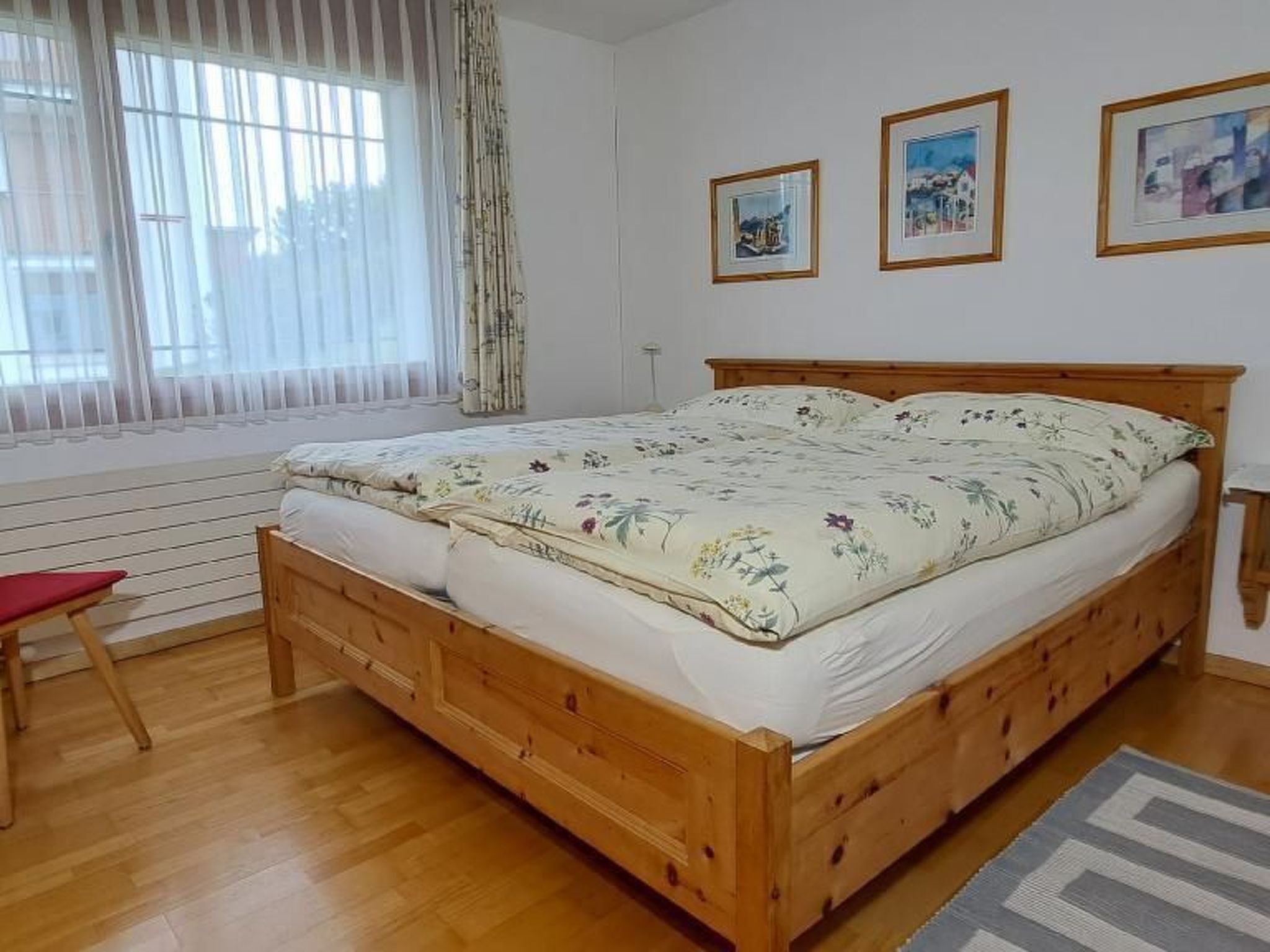 A bedroom with a wooden bed, a red chair, and three framed pictures on the wall.