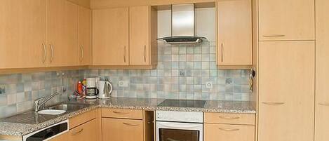 A kitchen with wooden cabinets, a tiled backsplash, a built-in oven, and a coffee maker.
