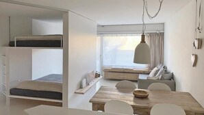 Un apartament estudi compacte amb un llit superposat, una zona de menjador i un gran finestral que deixa entrar molta llum natural.