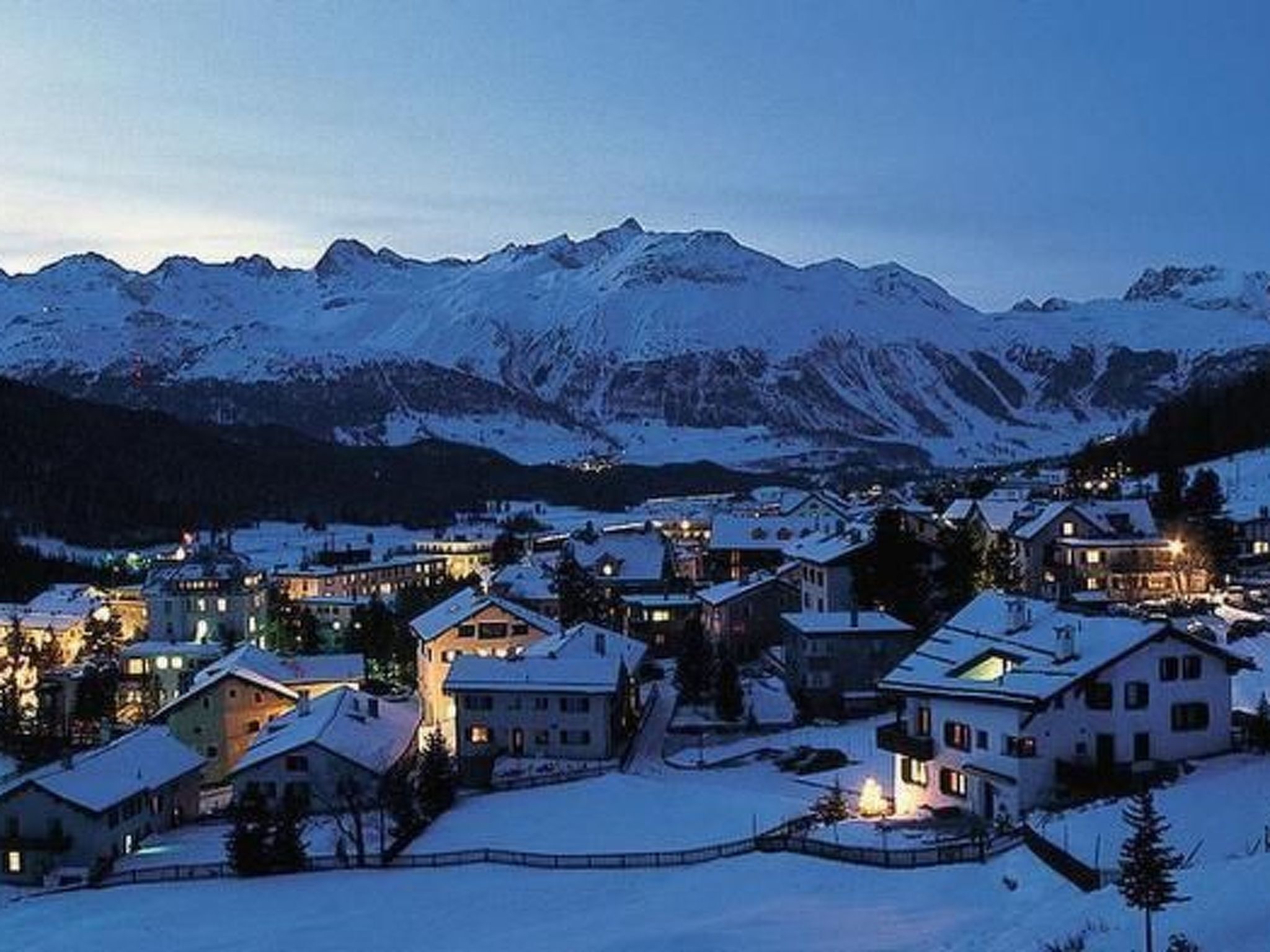 Un village enneigé, avec des maisons et une chaîne de montagnes en arrière-plan.