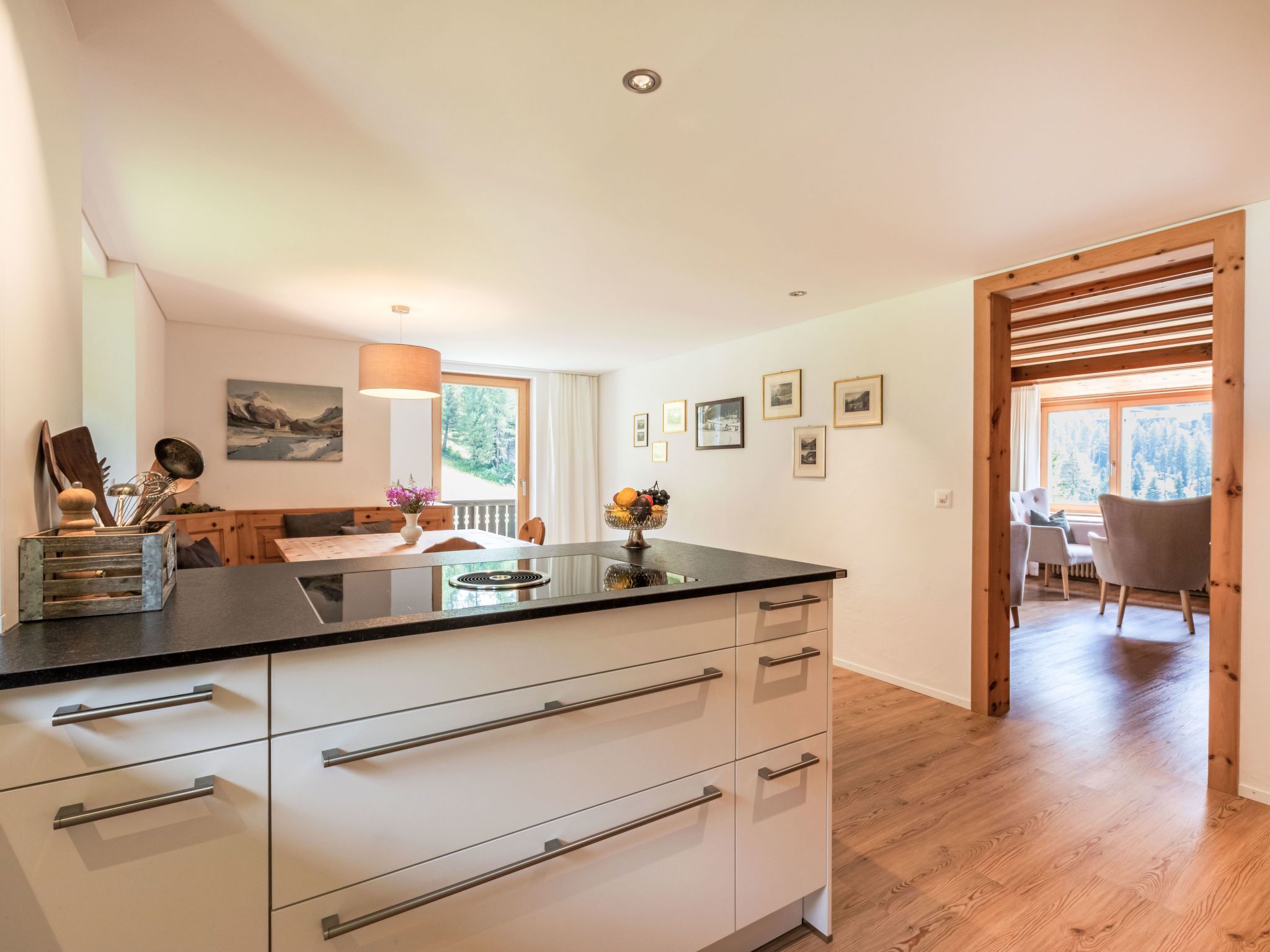A modern kitchen with a large island, wooden flooring, and a view of a dining area with a wooden ceiling.