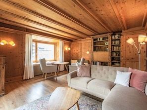 A cozy room with a wooden ceiling, a sofa, a dining table, and a bookshelf. - Chesa Kober - adults only by Interhome (Pontresina)
