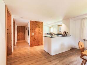 A modern kitchen with a wooden island, a dining table, and a view of the living area. - Chesa Kober - adults only by Interhome (Pontresina)